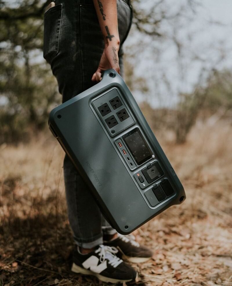 Person carrying a portable power station in rustic outdoor setting.