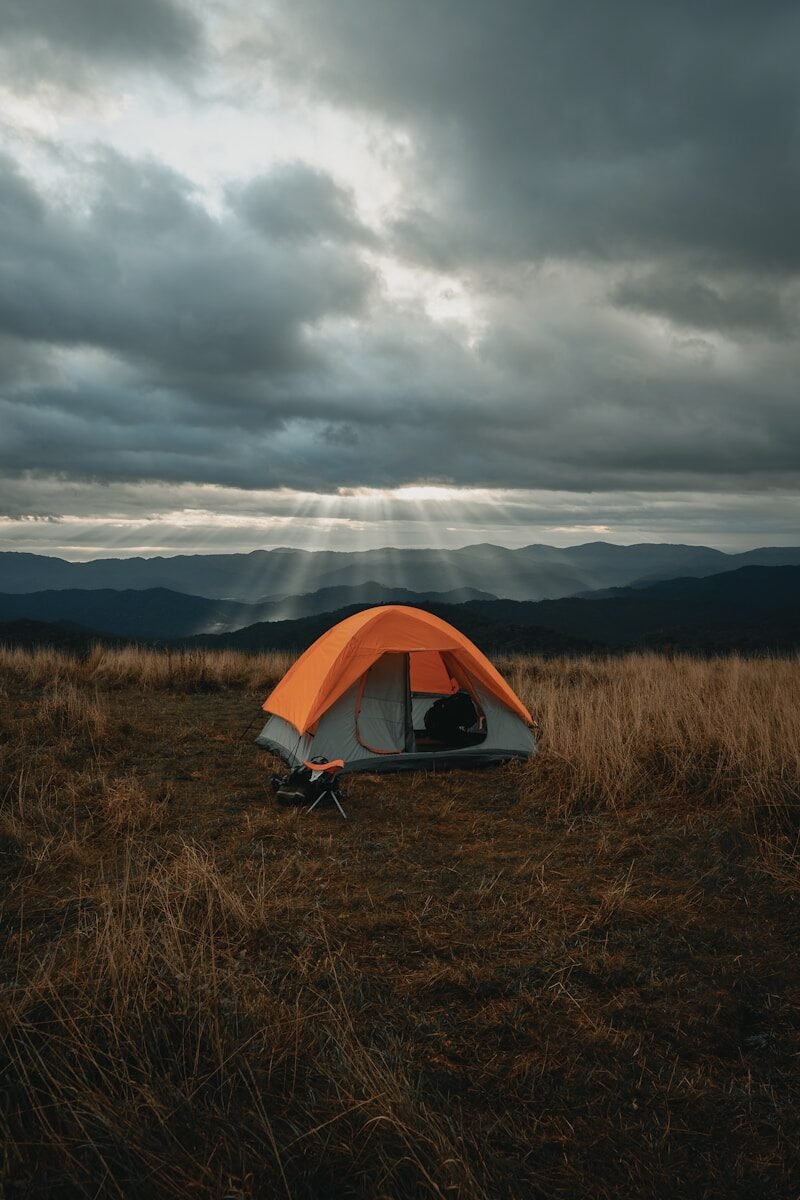 set-up gray and orange tent on brown field under cloudy sky