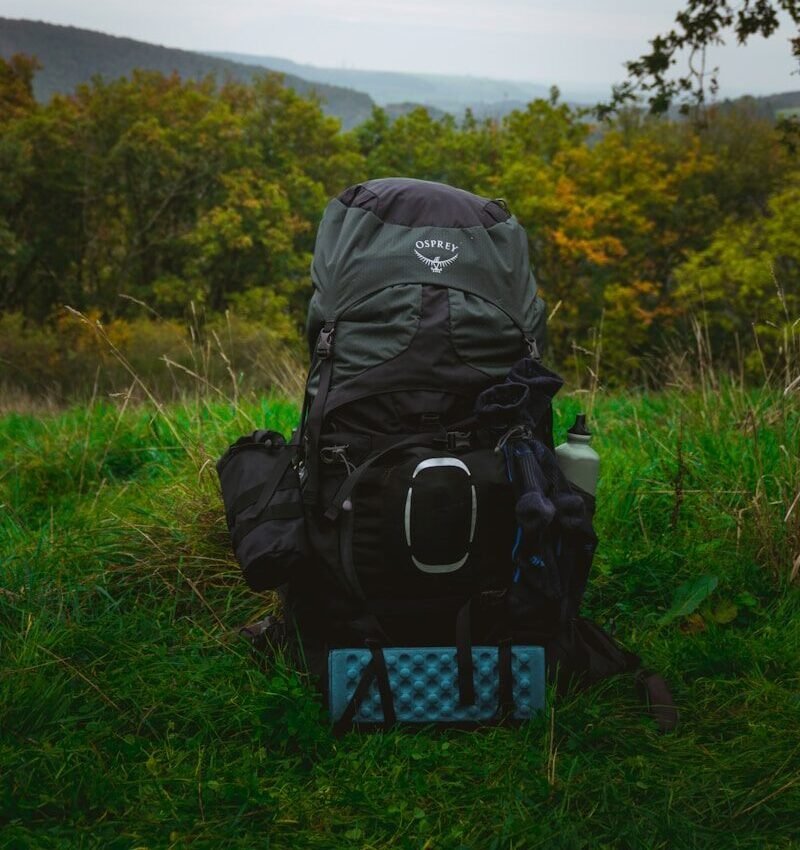 A large backpack sits on grassy ground with hills behind